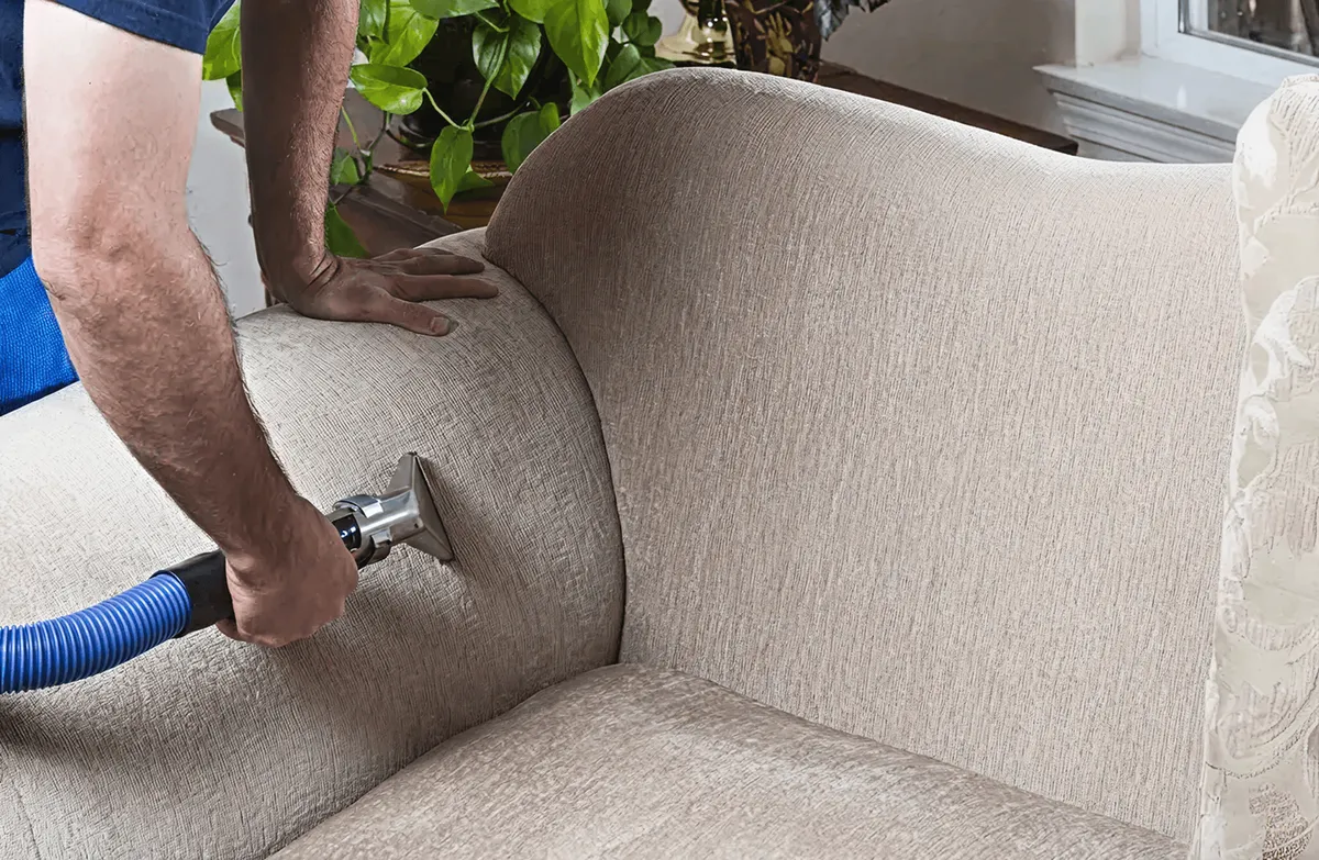 Professional upholstery cleaner deep-cleaning a fabric sofa with a handheld extraction tool and hose, Baton Rouge, LA.